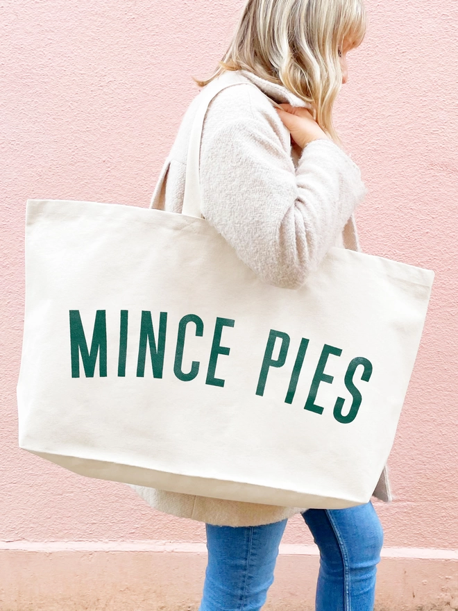 model carrying an oversized natural canvas tote bag with bold mince pies slogan