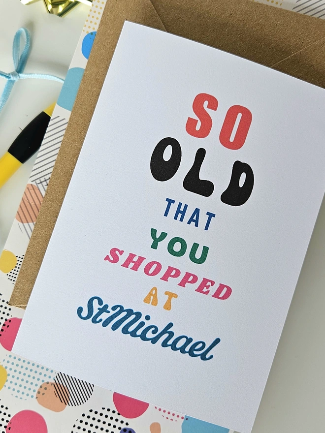 A photograph of the front of a humorous A6 greeting card illustrated using brightly coloured text and the retro shop logo. The text says so old you shopped at St Michael.