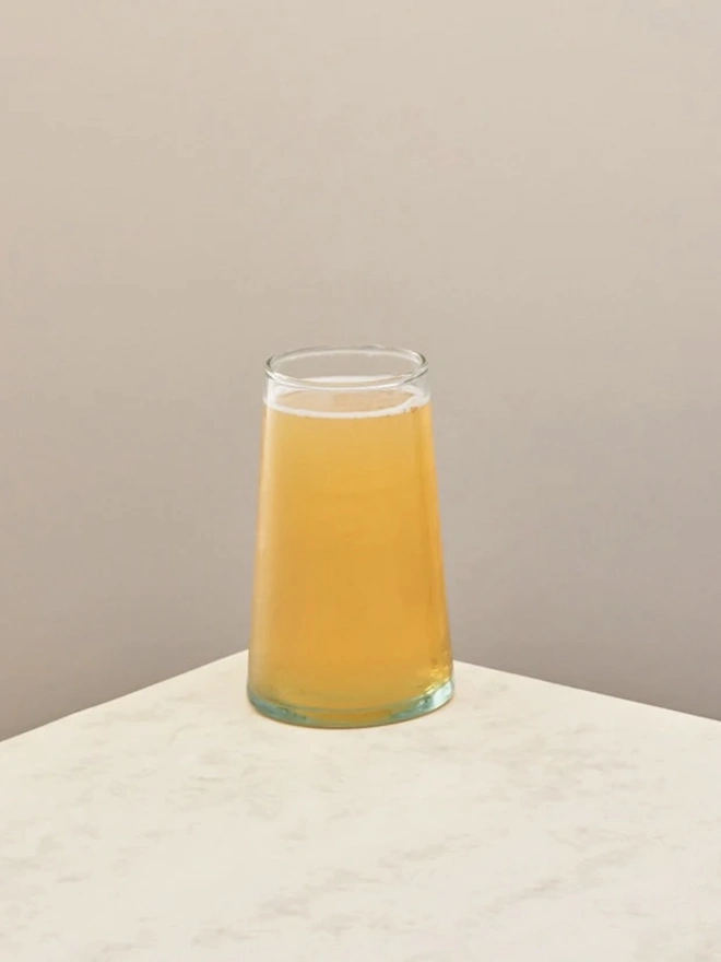 Highball Glasses (Set Of 1 Or 4), a highball glass sitting on a plain counter top against a white backdrop. It is filled with a soft drink. 