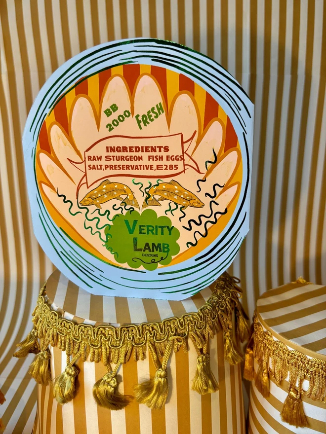 Salmon Round Tin Card, a colourful card sitting on a decorated display in front of a backdrop. 