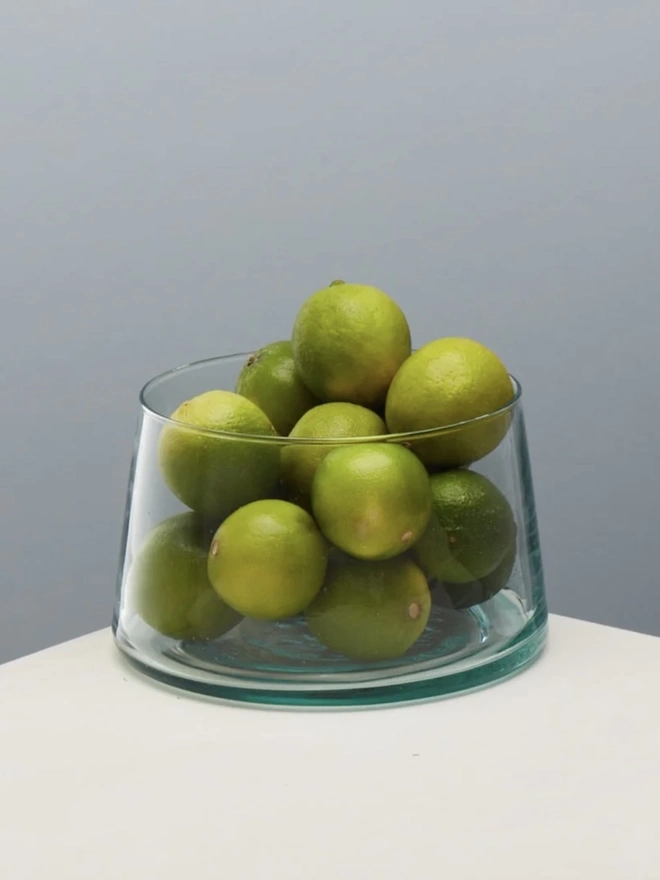 Tall Glass Dish, a tall glass dish sitting on a white surface against a baby blue backdrop. It is filled by olives. 