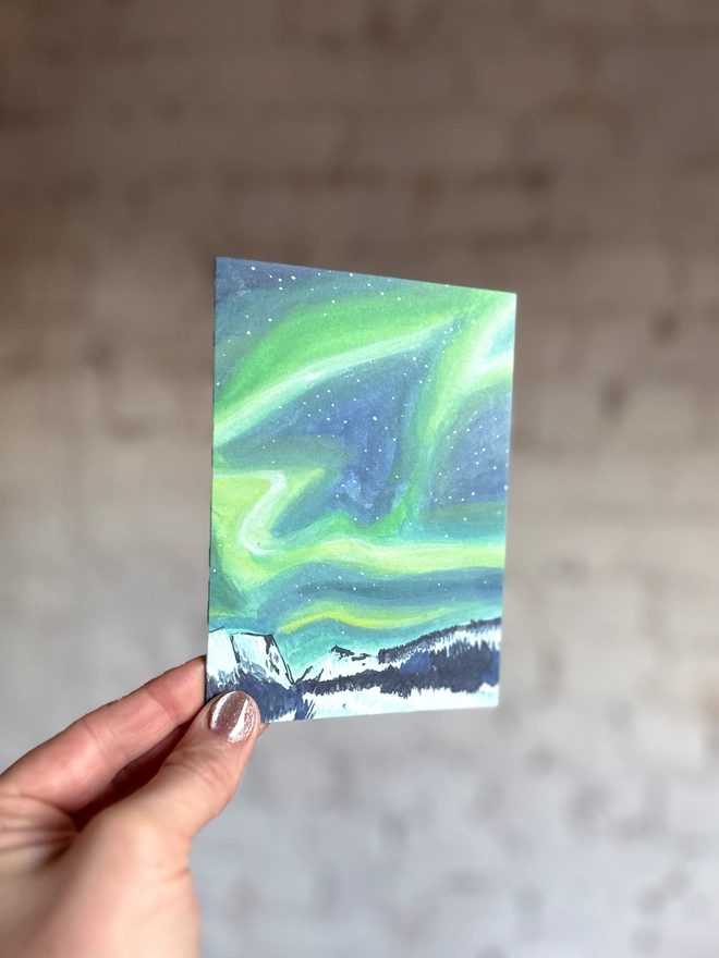 a greetings card featuring an illustration of the northern lights above a snowy landscape