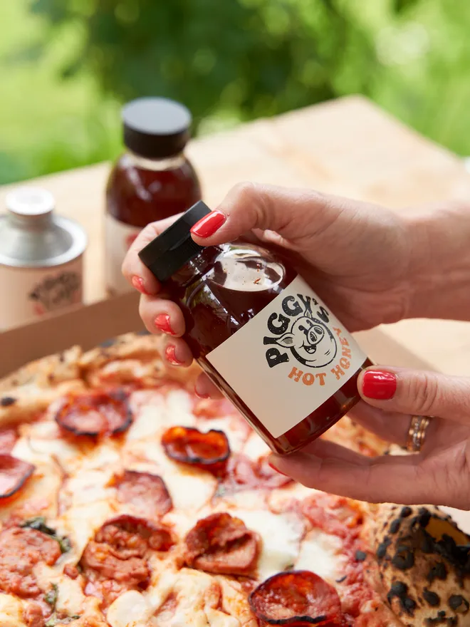 Piggy's Hot Honey- held up against a pizza in the garden 