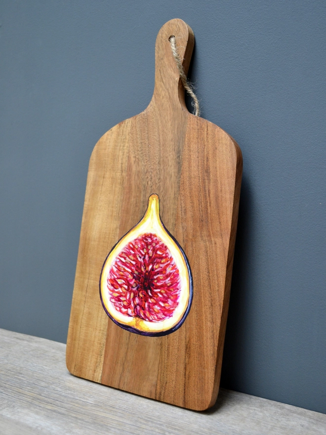 A wooden serving board with a handpainted design of a ripe fig