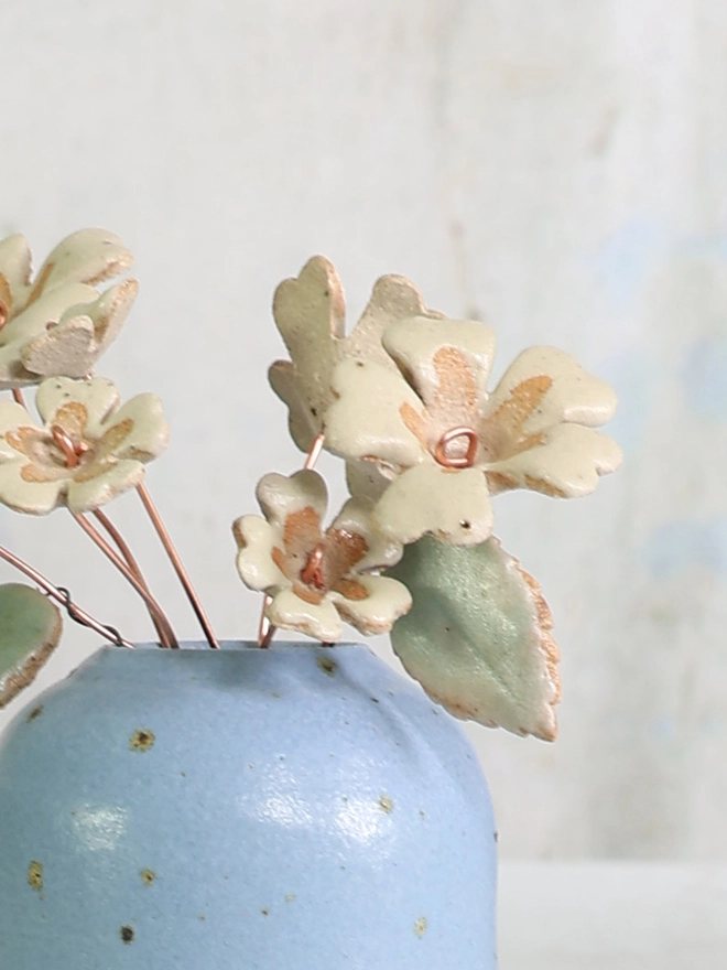 yellow ceramic primrose flowers arranged in a small blue stoneware vase