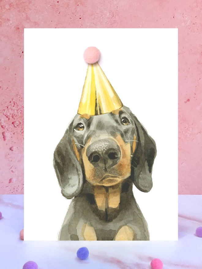 Black and Tan Dachshund Pompom Birthday Card in front of a pink background and surrounded by pompoms
