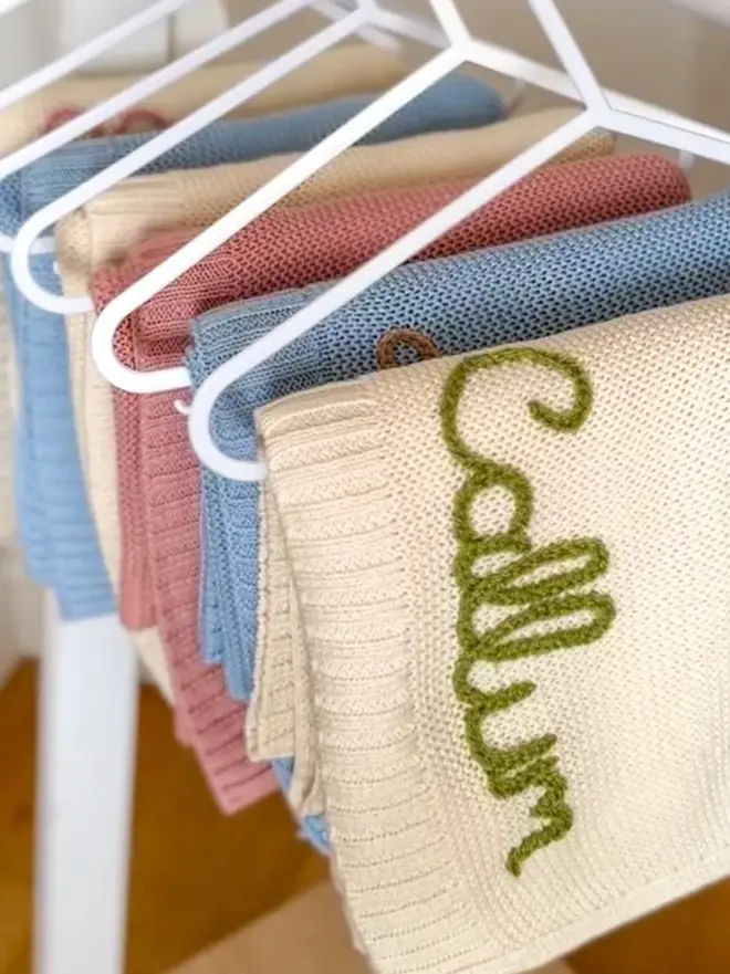 Hand Embroidered Baby Blankets, colourful embroidered blankets hanging in a group. They are personalised with names. 