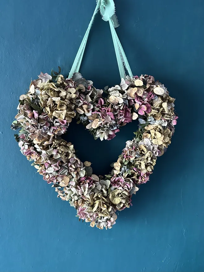 dried violet hydrangea heart shaped wreath. a heart shaped dried flower wreath hung up on a blue wall.
