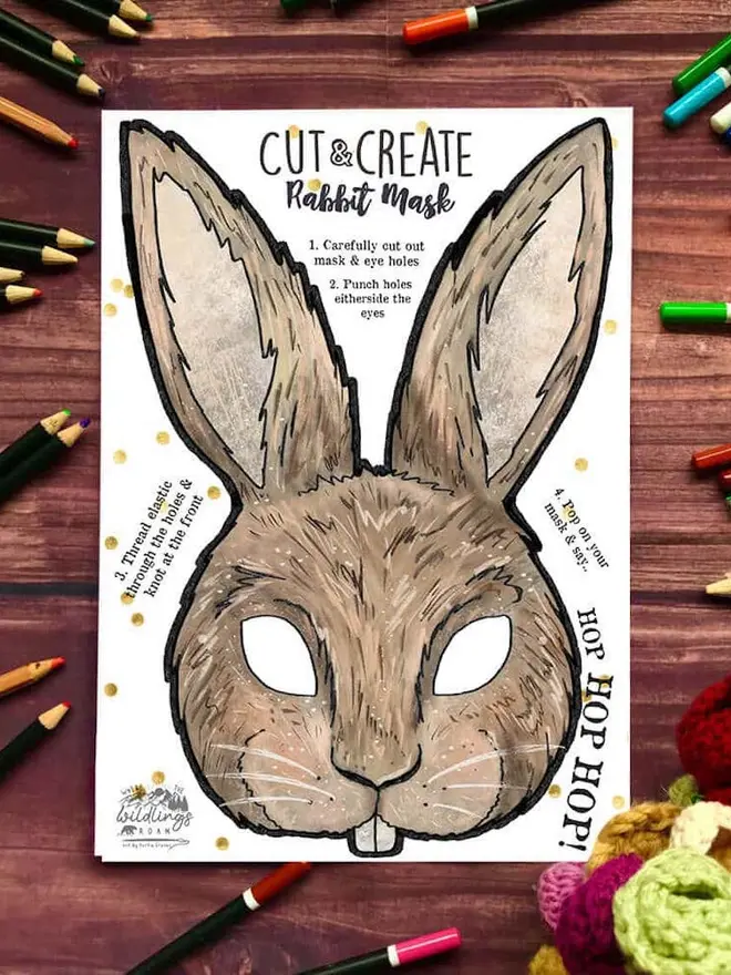 Cut And Create Forest Animals Children’s Masks Kit, an illustrated rabbit face, surrounded by coloured pencils on a dark wood background.