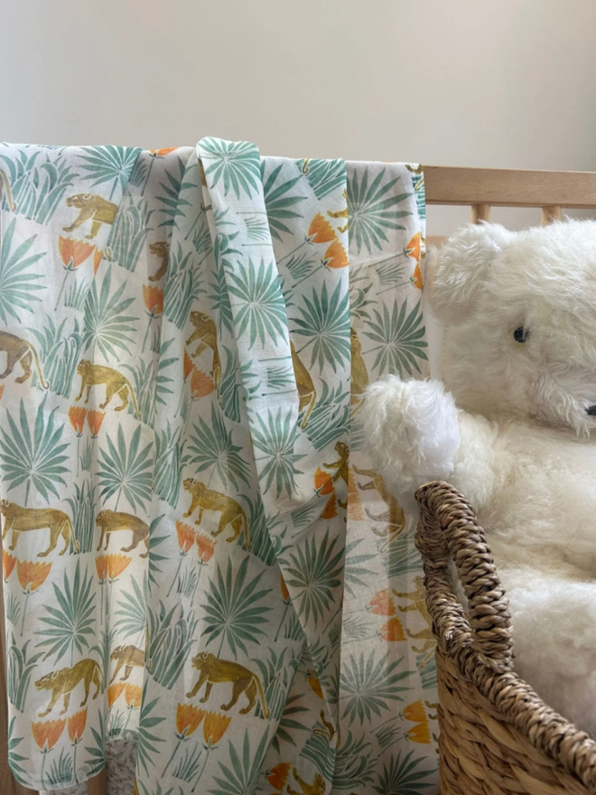 Lioness Amongst the Palms Muslin. A muslin patterned with lionesses in palm trees, draped on a chair.