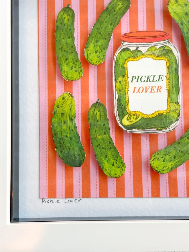 Charming framed collage featuring vibrant illustrated pickles, set against a colorful red and pink striped background, with gherkins and a pickle lover's jar. This vibrant and lovingly crafted mini collage is super cute and will delight pickle lovers and gherkin fans alike!