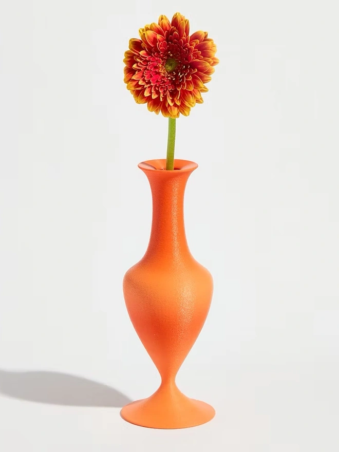 curvy shaped bright orange 3d printed vase holding orange flower