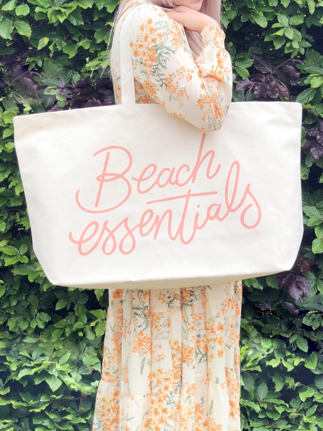 model holding an oversized natural canvas tote bag with beach essentials slogan