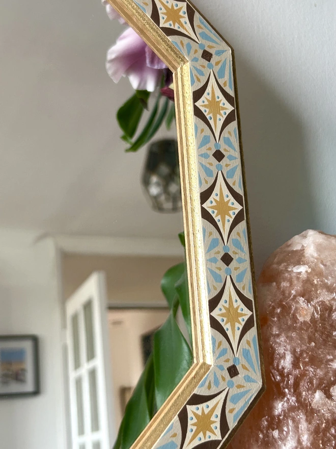 Medium sized octagonal wall mirror with a hand painted decorated frame with gold stars and blue star burst repeating pattern around the frame