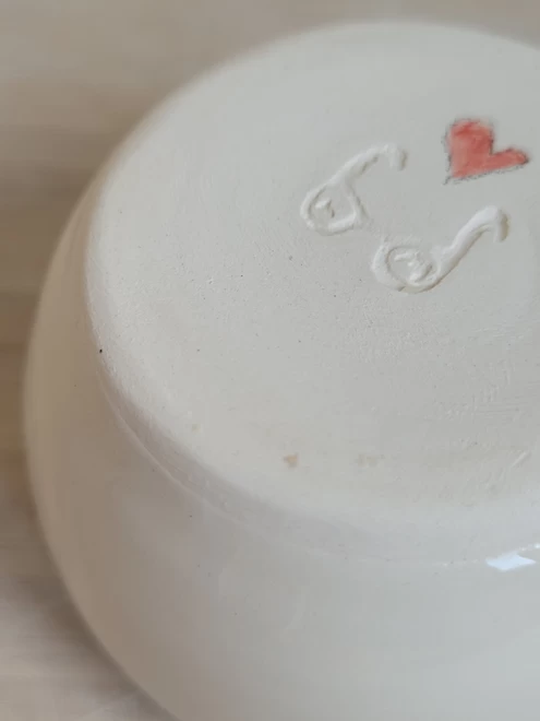 close up of the underneath of a white ceramic pot showing the maker's stamp and a small red heart