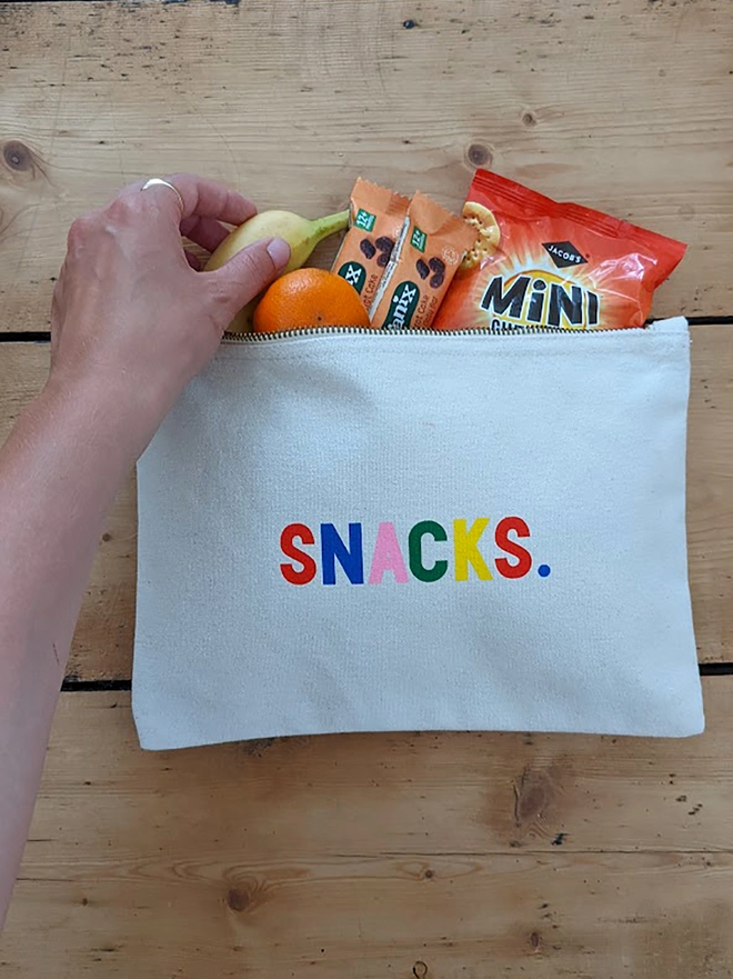 A canvas pouch on a wooden floor with multi coloured 'Snacks slogan