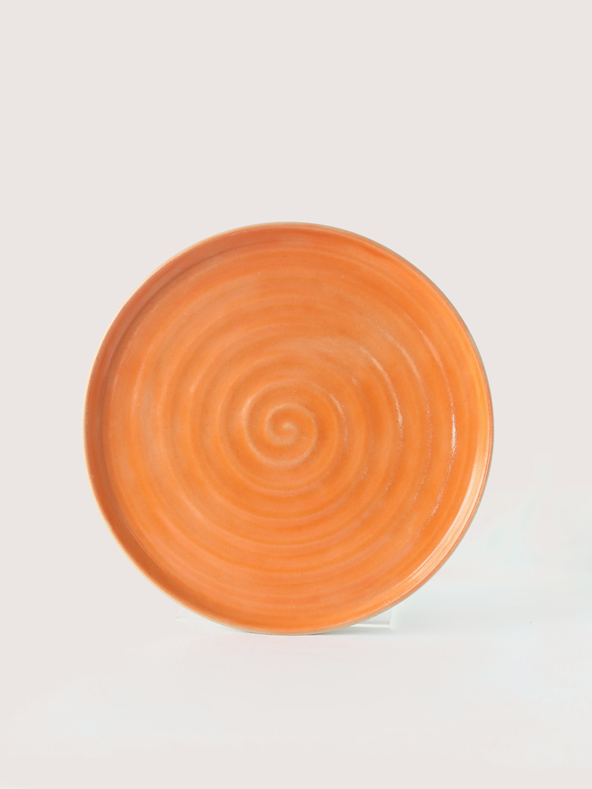A handmade ceramic side plate in mandarin orange glaze, photographed from the front against a plain white background, showing a natural concentric swirl texture from the wheel-throwing process