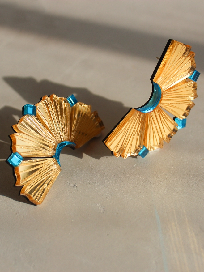 A still life image of pair of earrings in gold and Aqua. The earrings resembles like the coral walls of Lamu Island and sliced pineapple.