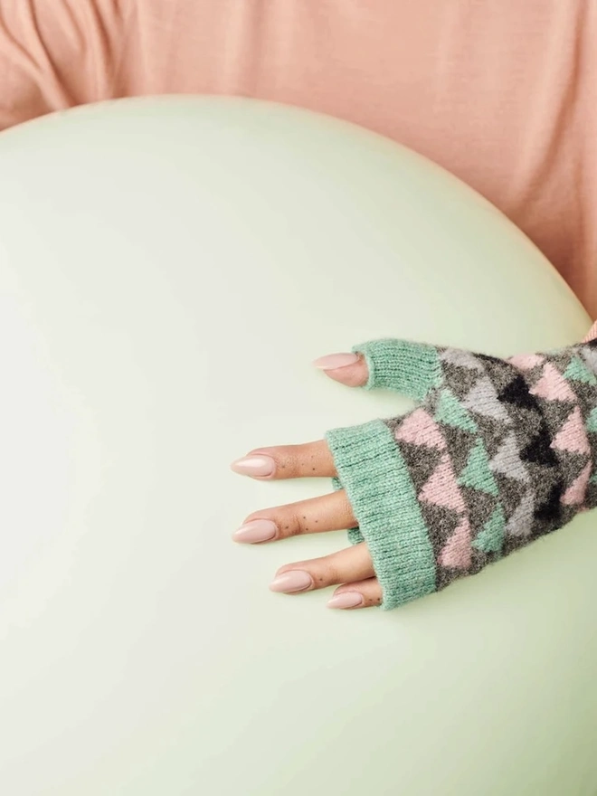 Women's Grey & Mint Triangle Lambswool Wrist Warmers, a woman wearing a pair of colourful wrist warmers inside. 