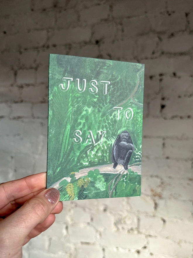a greetings card featuring an illustration of a chimp sitting in the jungle with the text “just to say”