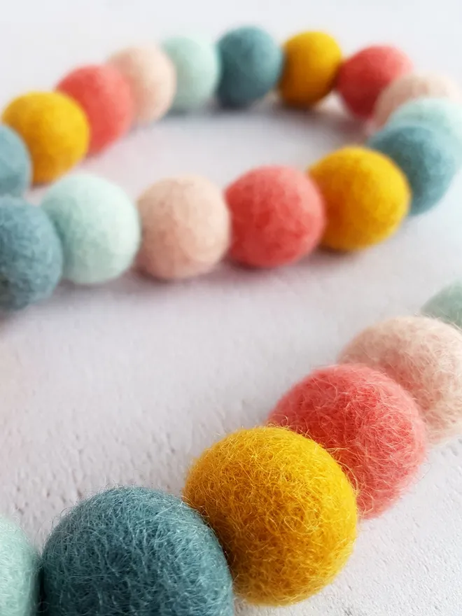 A pastel nursery felt ball bunting in bright colours..