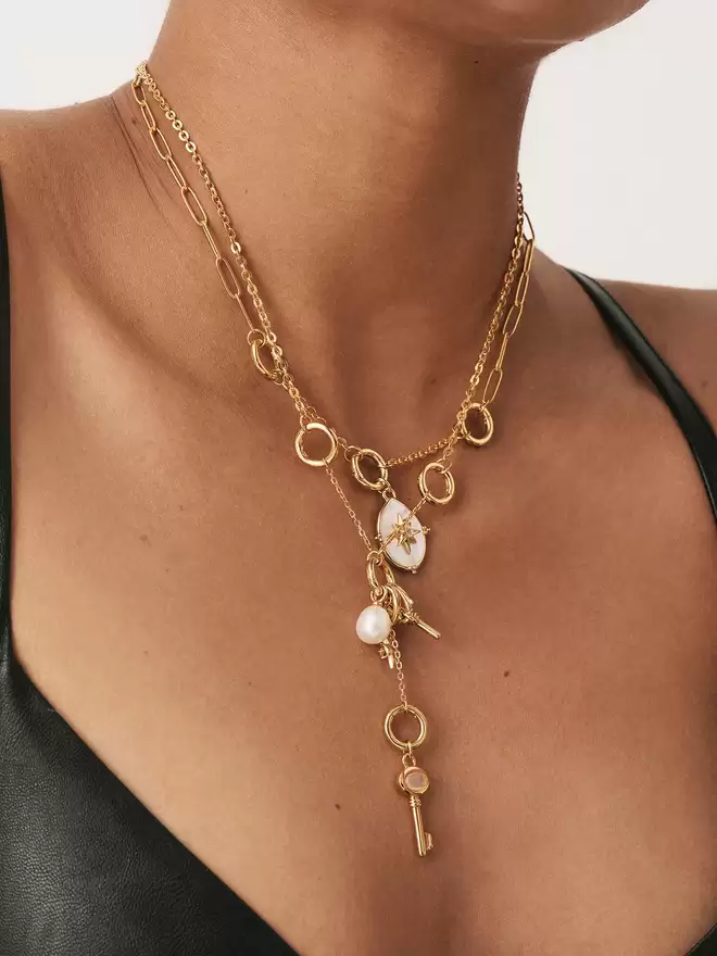 woman wearing two necklaces styled with a mother of pearl rose des vents pendant, a pearl amulet, a mini Albert gold charm and a skeleton key pendant with a moonstone