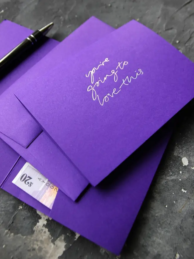 Hand foiled cash card or money wallet in a royal purple colour handfoiled in shiny holographic foil text which says ‘you’re going to love this’.