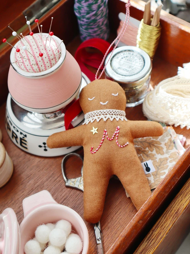 Brown linen gingerbread man christmas tree ornament with a letter hand embroidered in candy cane colours, star shaped sequin, crochet cotton lace around the neck, smile embroidered in white and candy cane colour string to hang. 