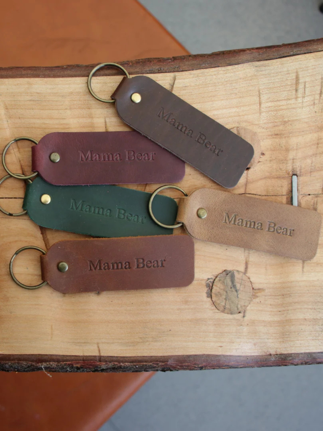 mother's day leather keyring. a selection of brown and green leather embossed keyrings, photographed on a wooden surface.
