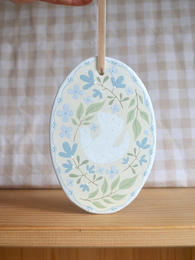oval ceramic decoration with white dove illustration and blue and green floral decor