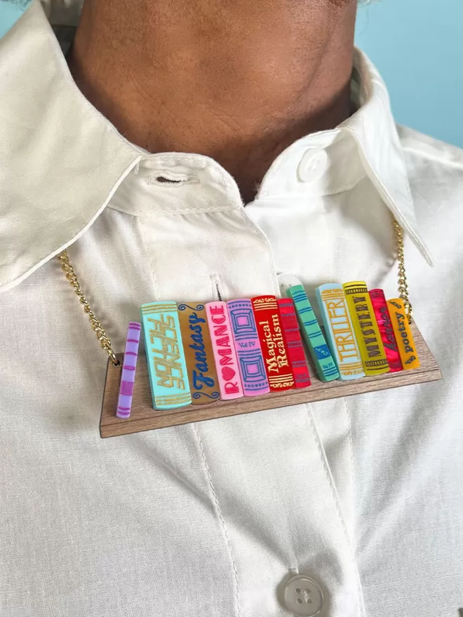 Close up of the tatty devine world book day bookshelf necklace worn over a collared white shirt.