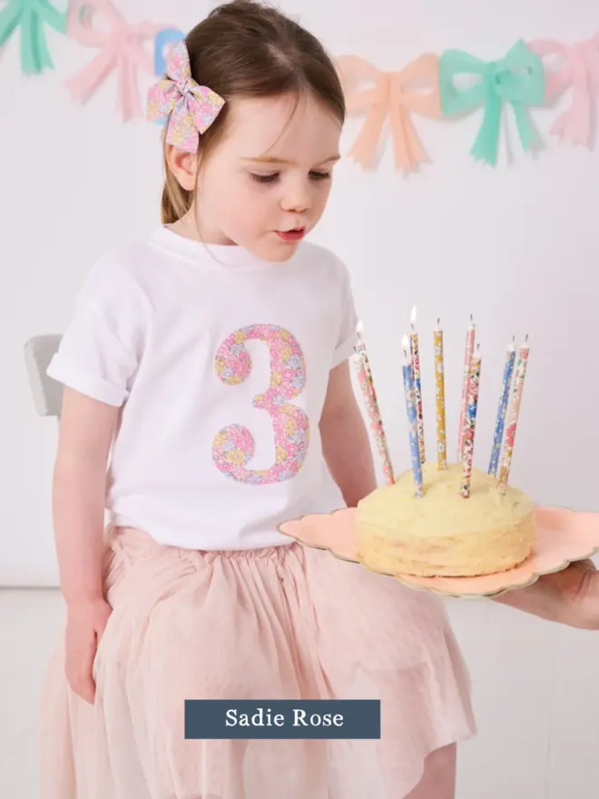 a 3 year old girl wearing a white birthday t-shirt with a number 3 cut from liberty floral print on the front