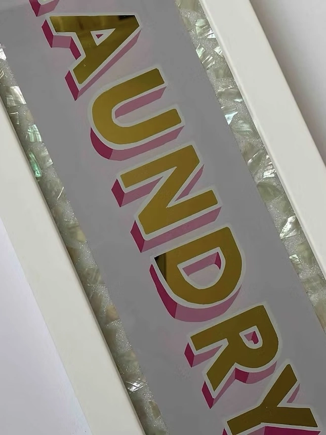 'Laundry' Glass And Gold Leaf Sign, a gold and glass sign sitting on a plain surface in a white frame. 