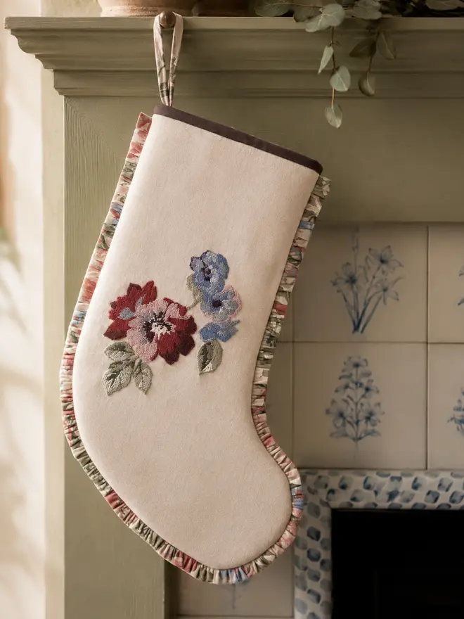 Rosa Chainstitch Ivory wool stocking with vintage chintz floral frill. Styled on a sage green wooden fireplace with vintage blue and white floral tiles.