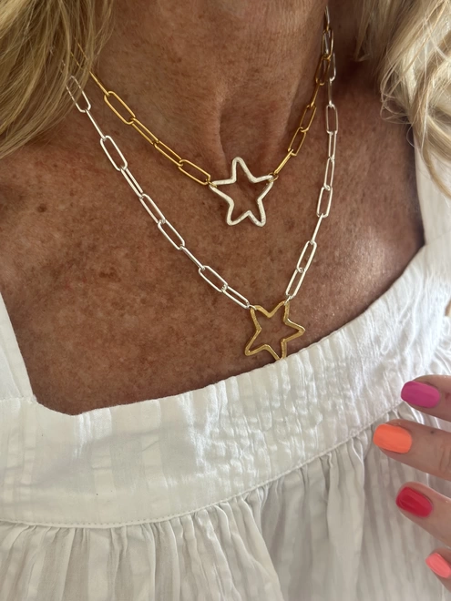 model wears rough hewn open star charm in gold on a sterling silver paperclip chain and rough hewn sterling silver open star charm on gold paperclip chain