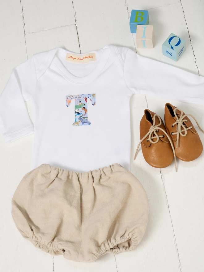 A baby bodysuit with long sleeves and an initial on the front in Liberty zoo animal print