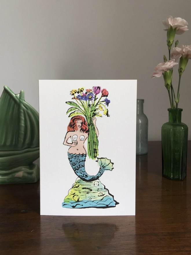 A greeting card featuring a beautiful smiling mermaid holding a wild flower posy bouquet! 