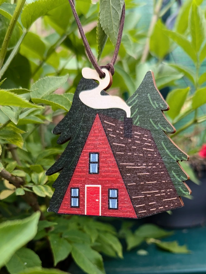 red cabin wooden Christmas decoration with a smokey roof and 2 pine trees