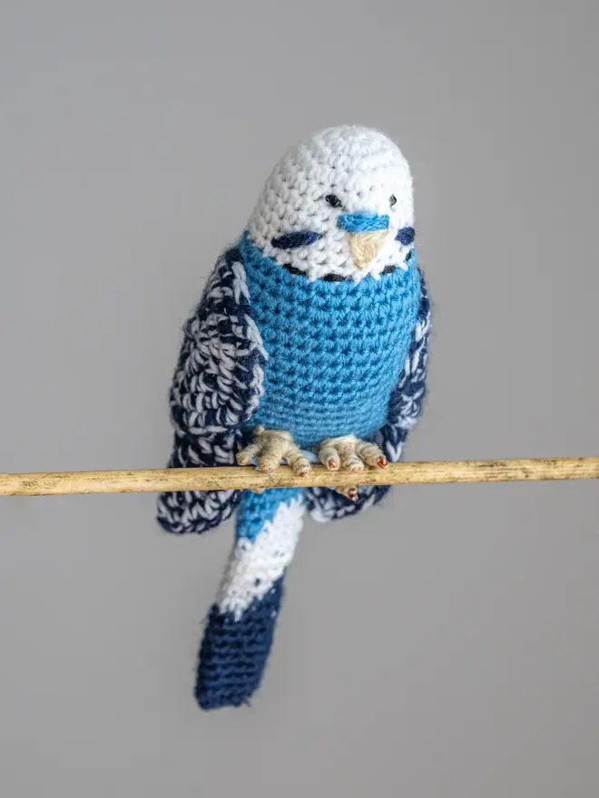Budgerigar Hand Crocheted Figure, a blue  crocheted bird sitting on a wooden poll. 
