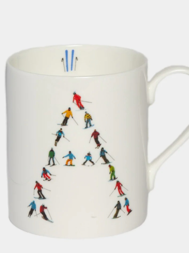 A simple white mug illustrated with an ‘A’ made of small, multicoloured skiers. The mug is set against a plain, white background.