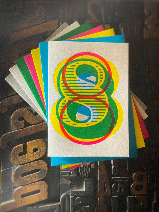 Handmade letterpress 8th birthday card featuring bold overlapping numerals printed in vibrant fluorescent cyan, magenta and yellow inks. Each card is individually hand printed using traditional letterpress techniques on luxury paper stock, creating a beautifully tactile finish with a deep impression and rich layered colours inspired by the CMYK printing process. Printed on a traditional letterpress from 1915. A wonderful artisan printed birthday card.