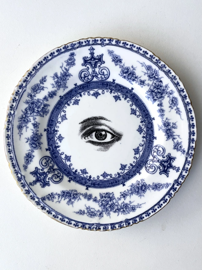 a really ornate plate with blue white florals and patterns, in the centre is printed a black and white illustration of a lovers eye