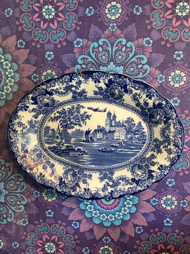 Classic blue and white patterned plate featuring a castle and river with boats sailing along. A Jet2 plane flies high in the sky.