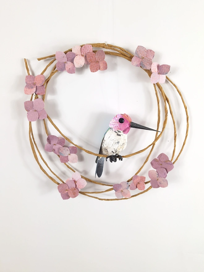 Anna's hummingbird sculpture, perched on a spring wreath adorned with purple hydrangea blooms