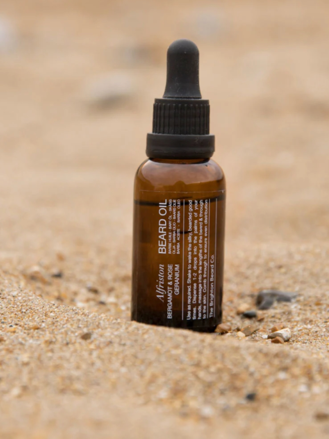 Alfriston Bergamot & Rose Geranium. A bottle of beard oil on a beach.