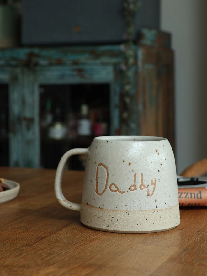 Personalised Kids' Handwriting Handmade Stoneware Mug with the name 'Daddy' on a wooden table 