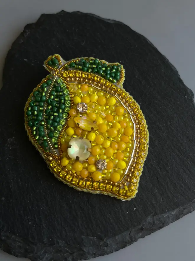 Lemon Beaded Brooch, placed in a black slate in the shape of a heart, against a white background. 