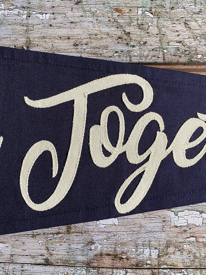 Detail of a navy canvas 'Better Together pennant flag. This shows the letters Toge written in ivory canvas.