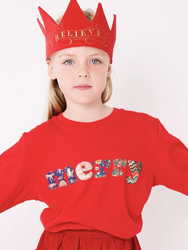 a 5 year old wearing a red christmas cotton t-shirt with the word merry hand cut from festive Liberty prints and appliquéd on the front