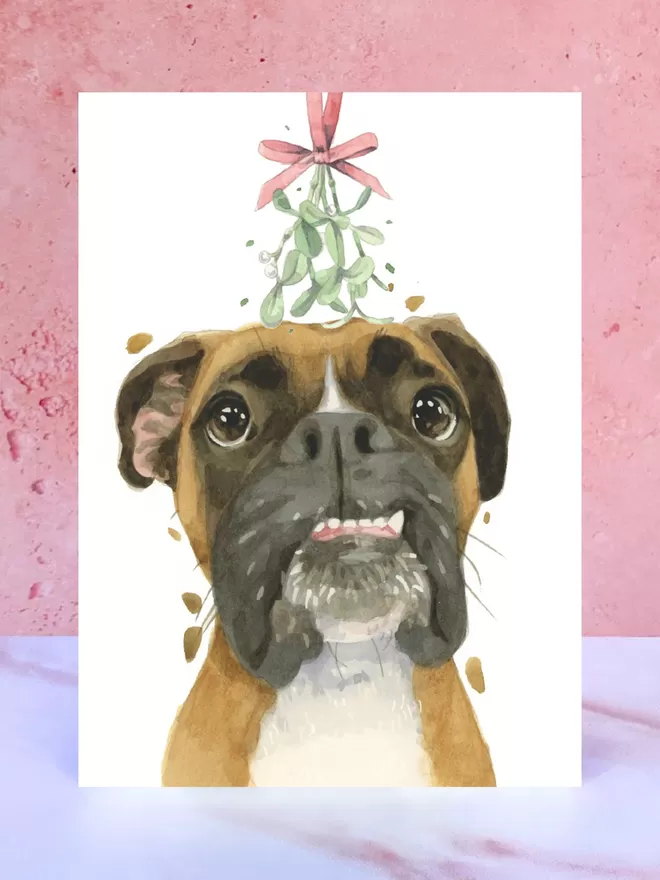 A Christmas card featuring a hand painted design of a Boxer Dog, stood upright on a marble surface.